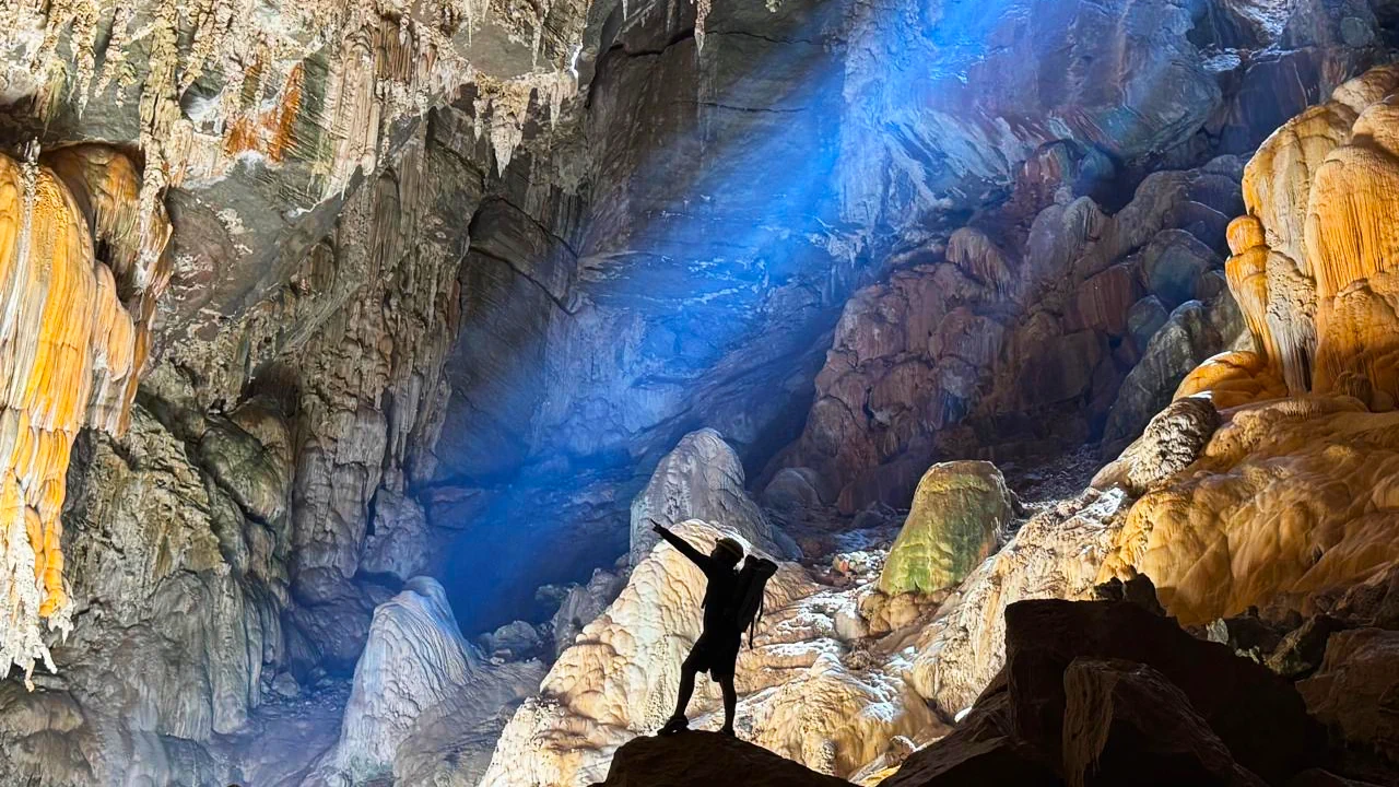 Explorer inside the massive Terra Ronca cave system in Brazil illuminated by natural light beams